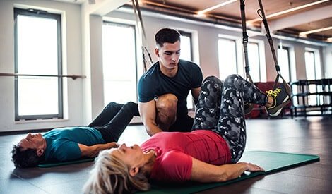 Entraîneur aidant une femme lors d'une séance de physiothérapie ou réadaptation sportive dans un centre de remise en forme moderne.