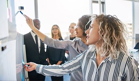 Filles et femmes d'affaires en réunion utilisant un tableau blanc interactif pour présentation et collaboration dans un bureau moderne.
